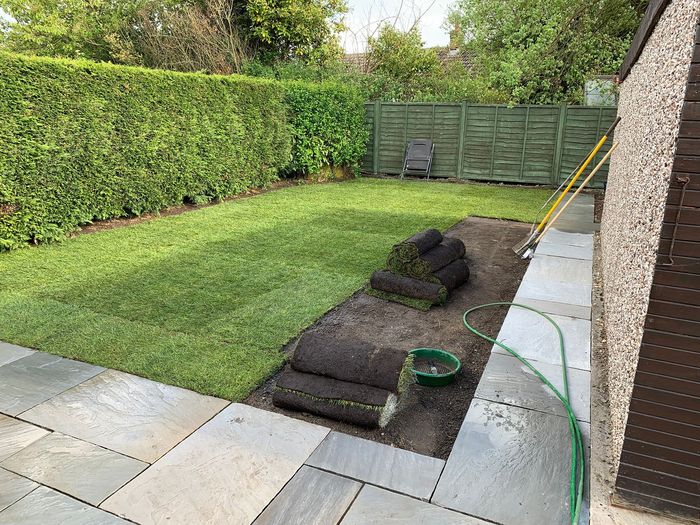 A lawn with rolls of turf and a hose in the middle of it.