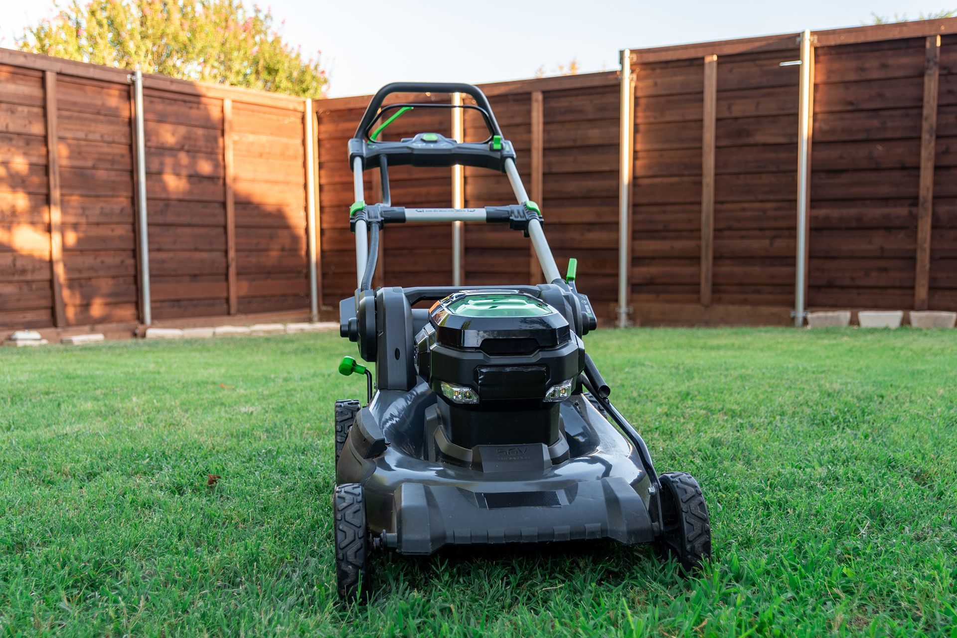 A lawn mower is sitting on top of a lush green lawn in front of a wooden fence.