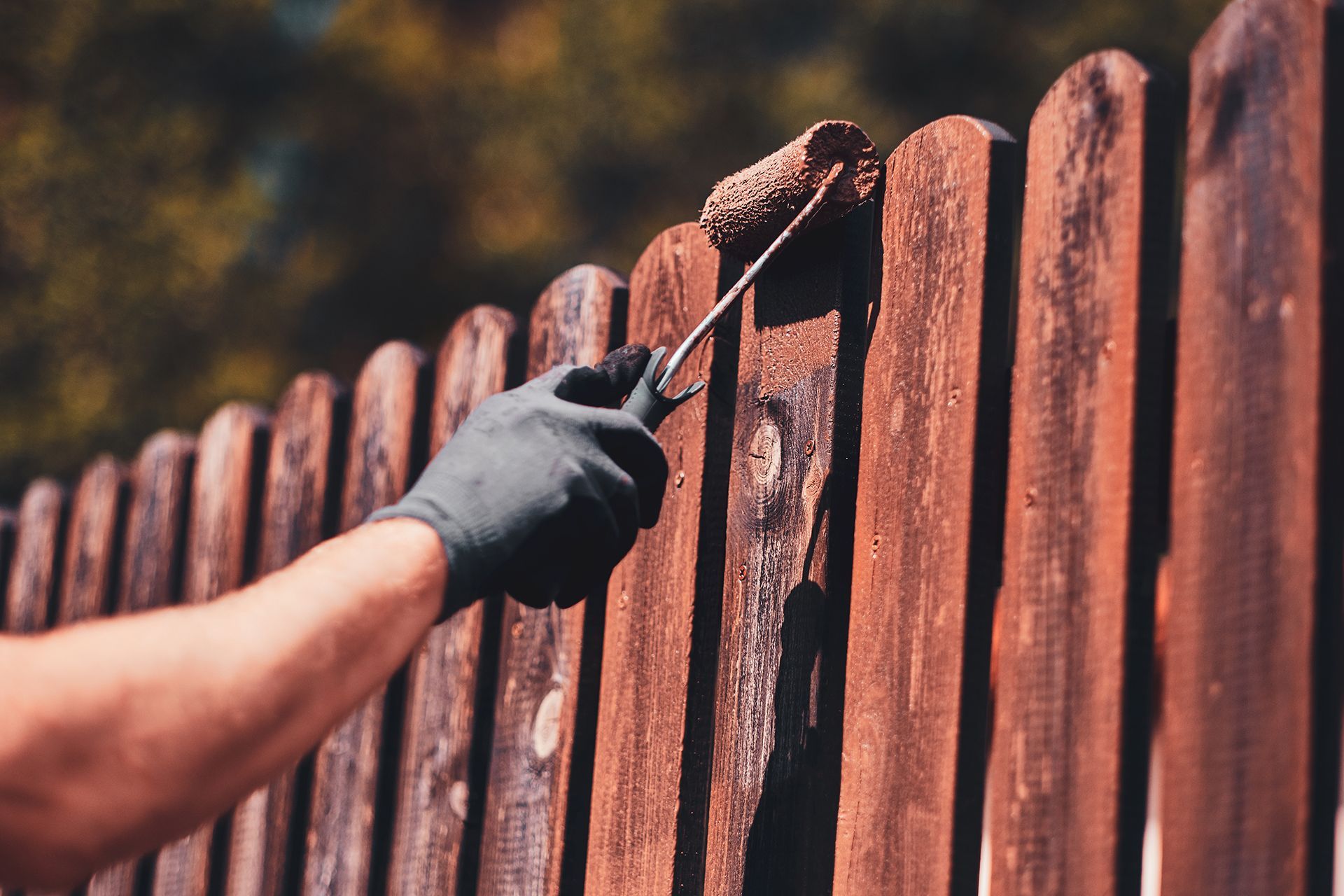 A person is painting a wooden fence with a roller.