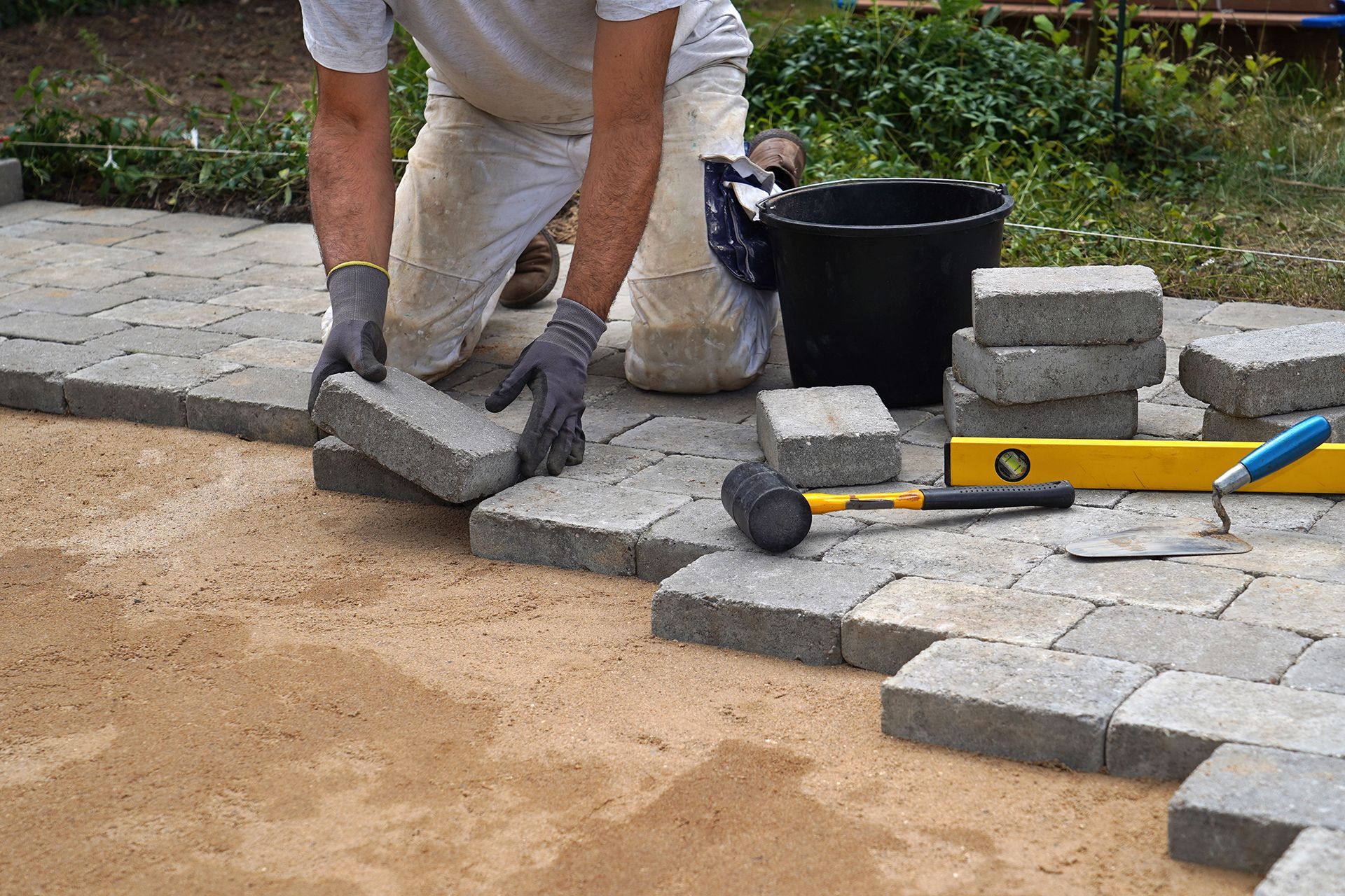 A man is laying bricks on a patio.