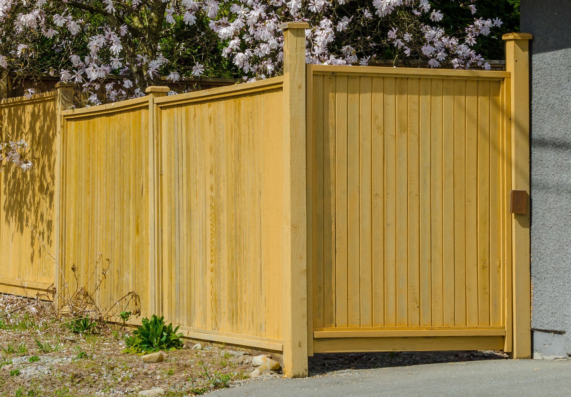 A wooden fence with a gate and flowers in the background.