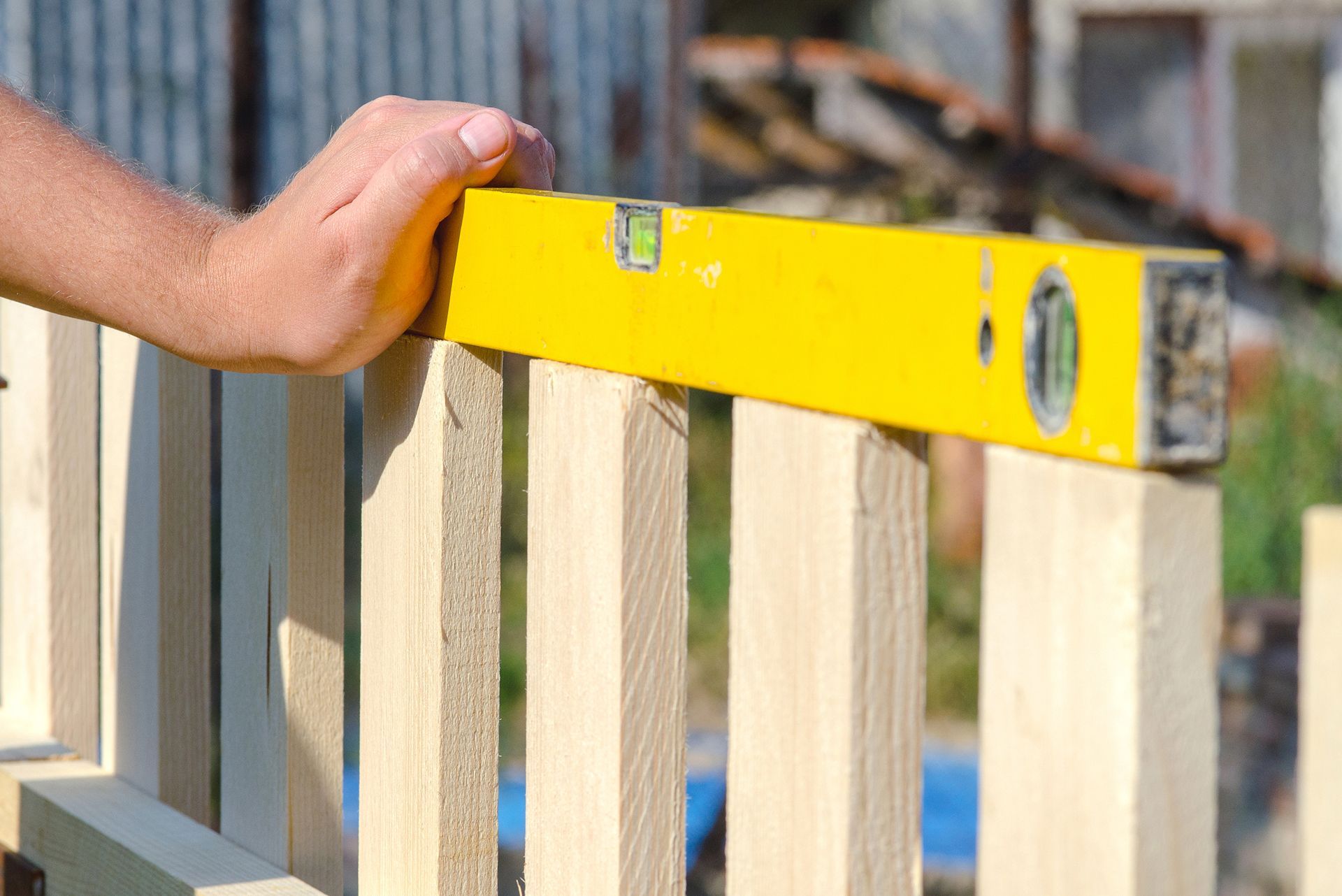 A person is measuring a wooden fence with a yellow level.