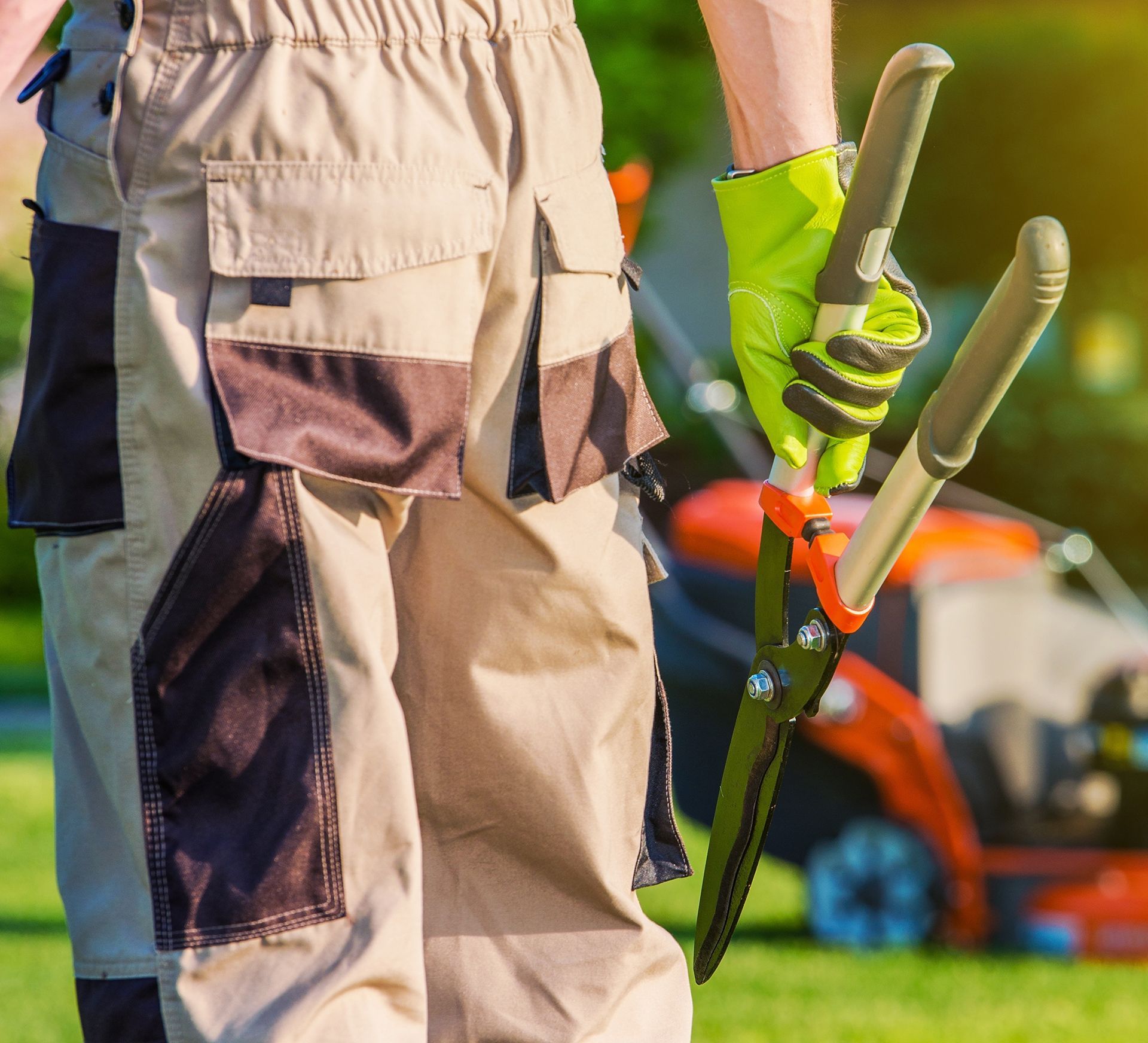 A man is holding a pair of scissors in front of a lawn mower