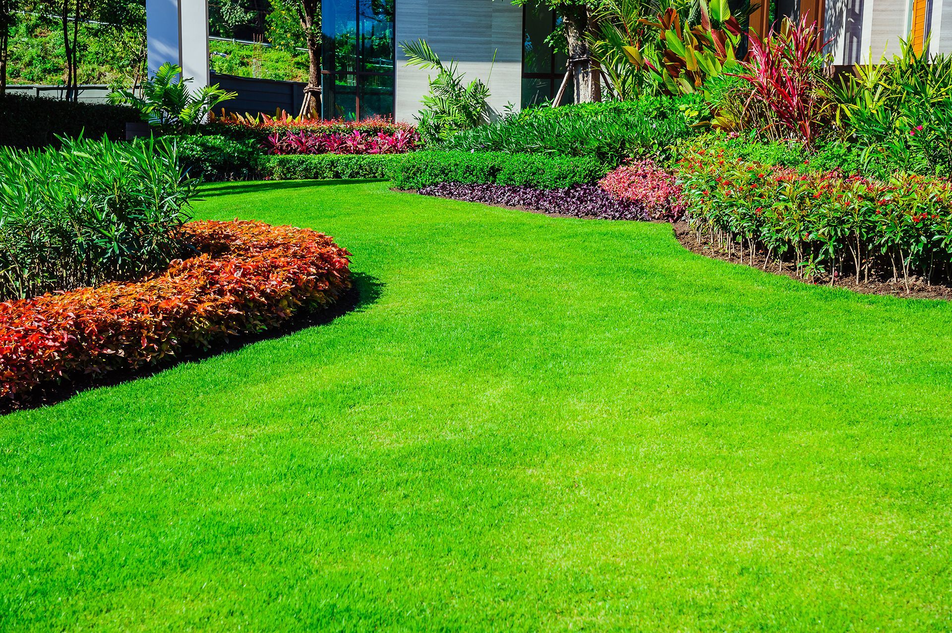 A lush green lawn with flowers and bushes in front of a house.