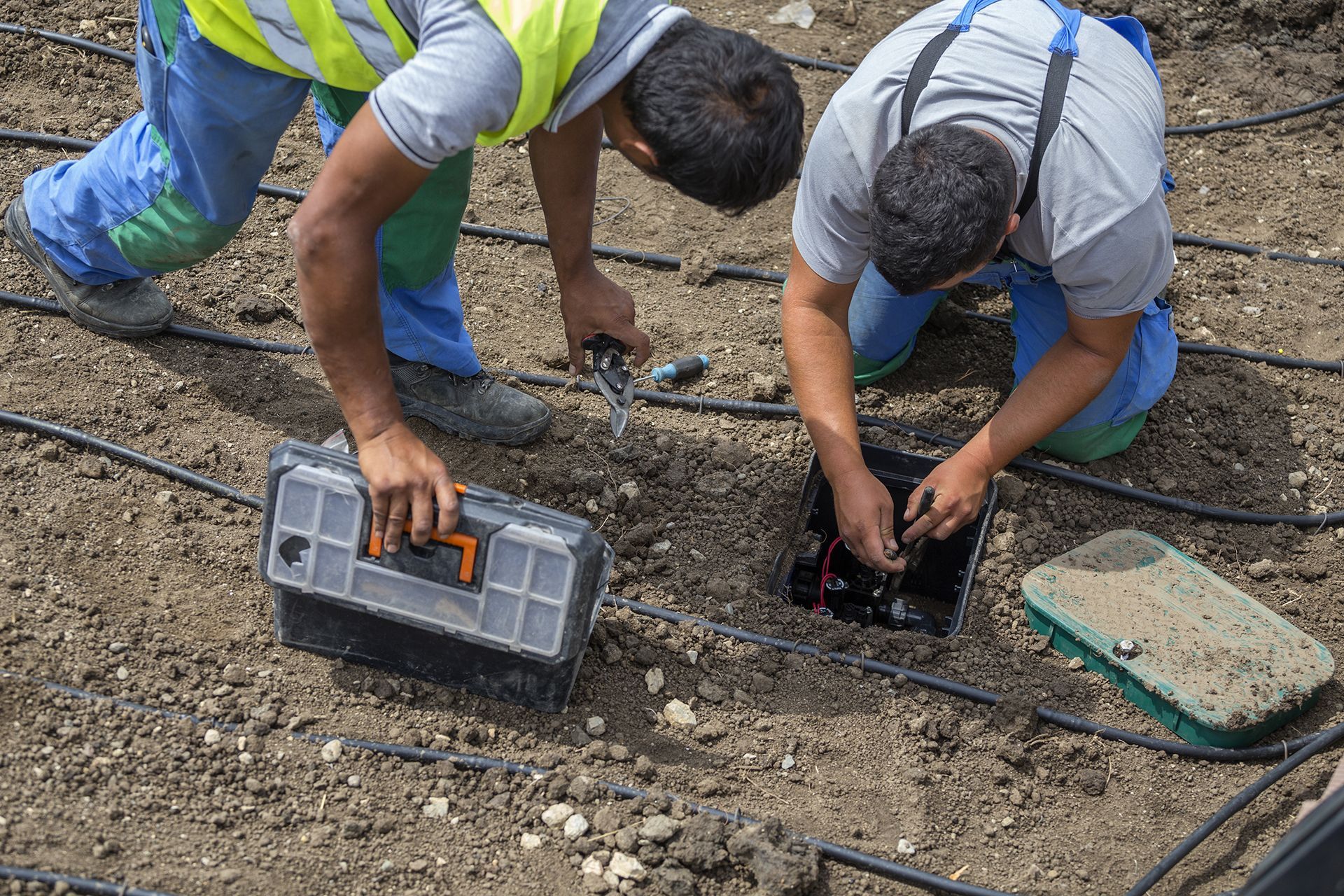 Two men are working on a irrigation system in the dirt.