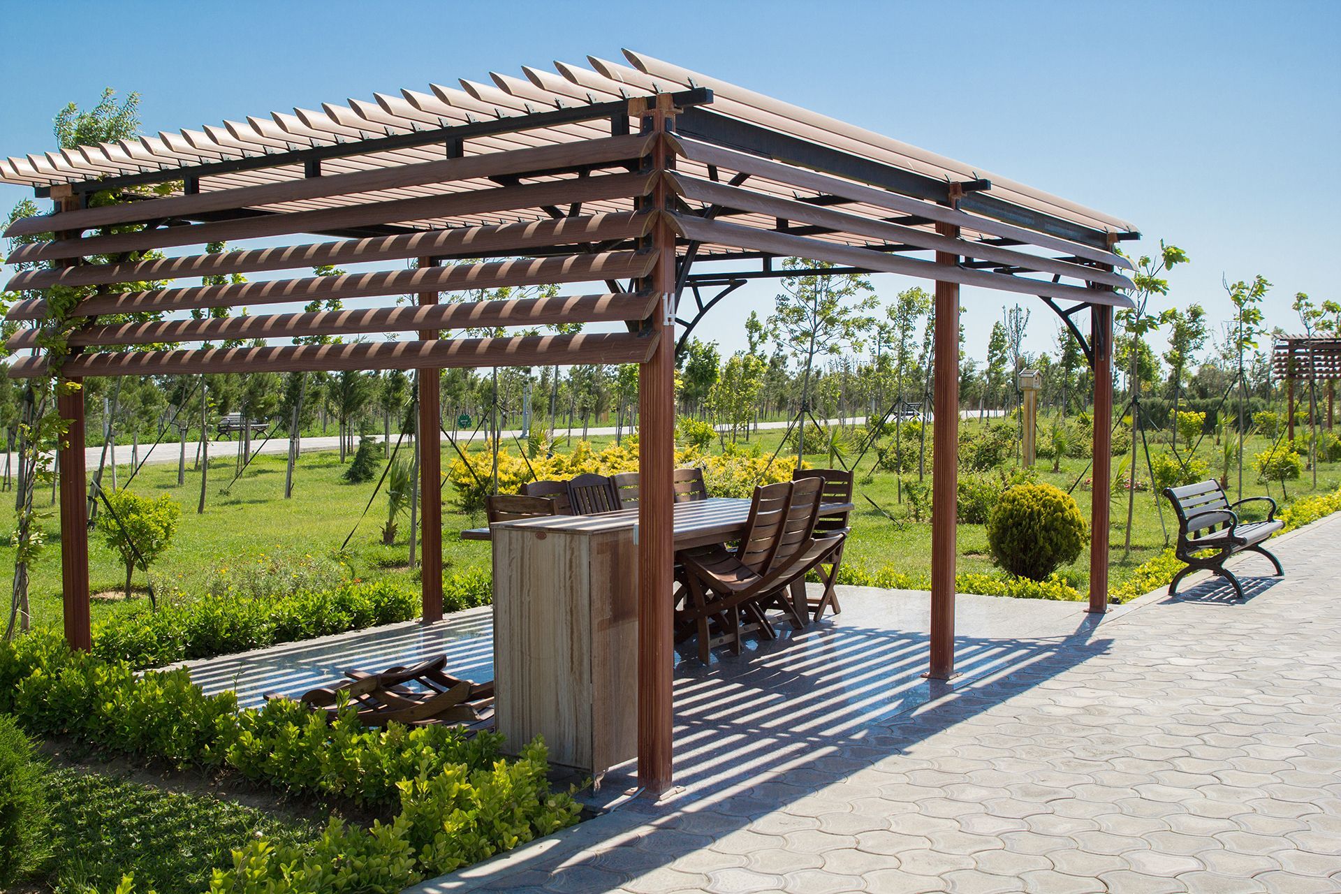 A wooden pergola with a table and chairs underneath it in a park.