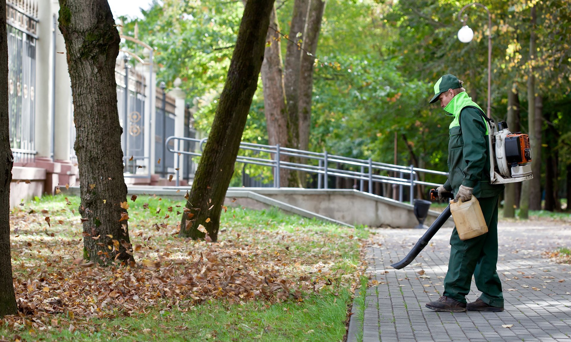 A man is blowing leaves from the sidewalk in a park.