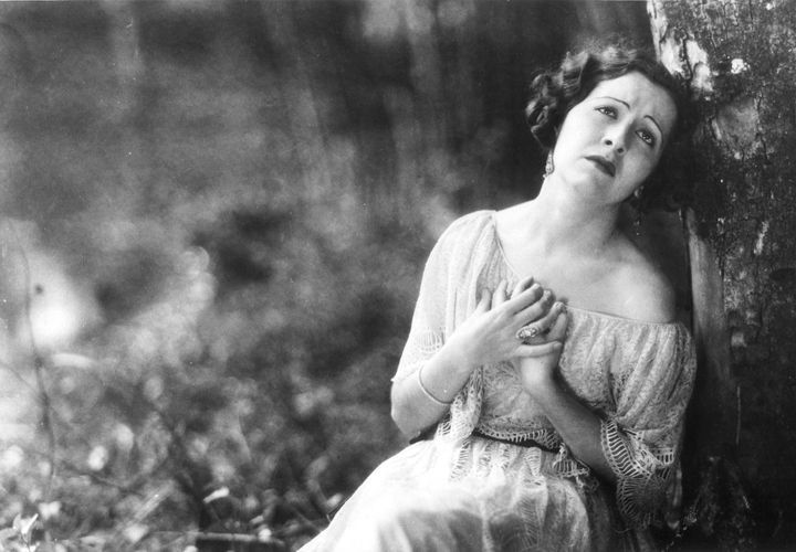 Uma foto em preto e branco de uma mulher encostada em uma árvore.