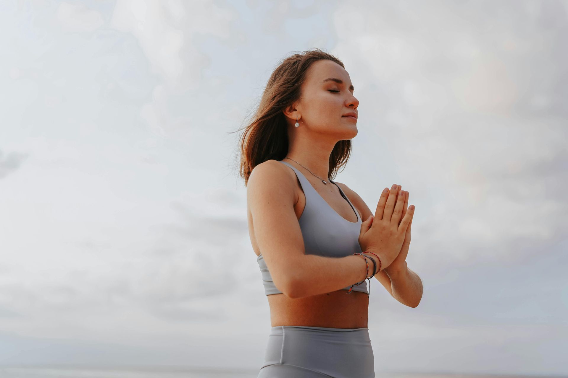 Une femme pratique le yoga sur la plage, les mains jointes en prière.