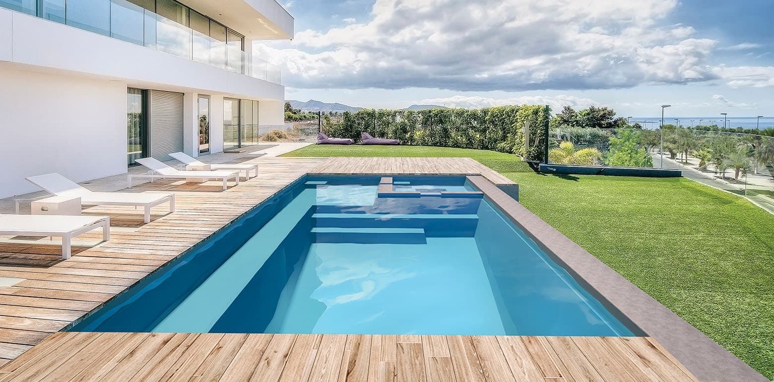 Modern white villa with a blue backyard pool, patio lounge chairs, and green lawn under a cloudy sky