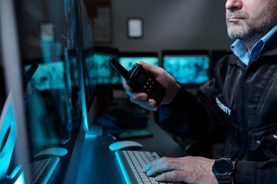 Vertriax security operations expert monitors surveillance feeds while coordinating via radio in control room.