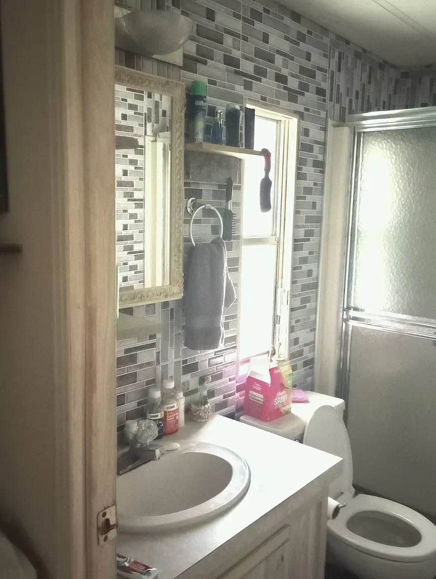 Bathroom with mosaic tile wall, sink, toilet, mirror, and shower.