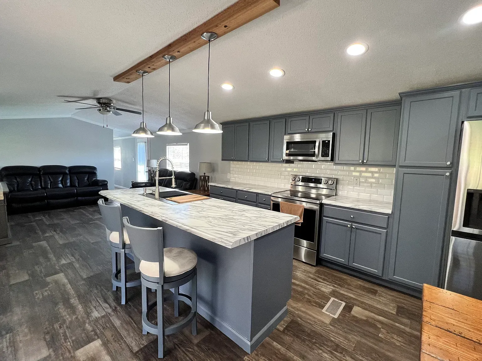 Modern kitchen with grey cabinets, island with stools, and stainless steel appliances.