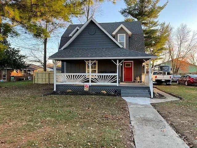 A dark gray house with a red door and white porch, set on a lawn with a walkway.