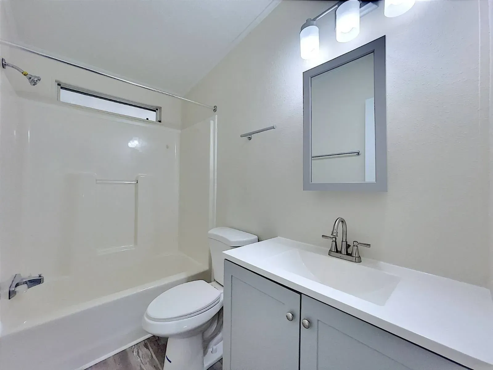 Bathroom with white bathtub, toilet, gray vanity, and mirror. Bright lighting.