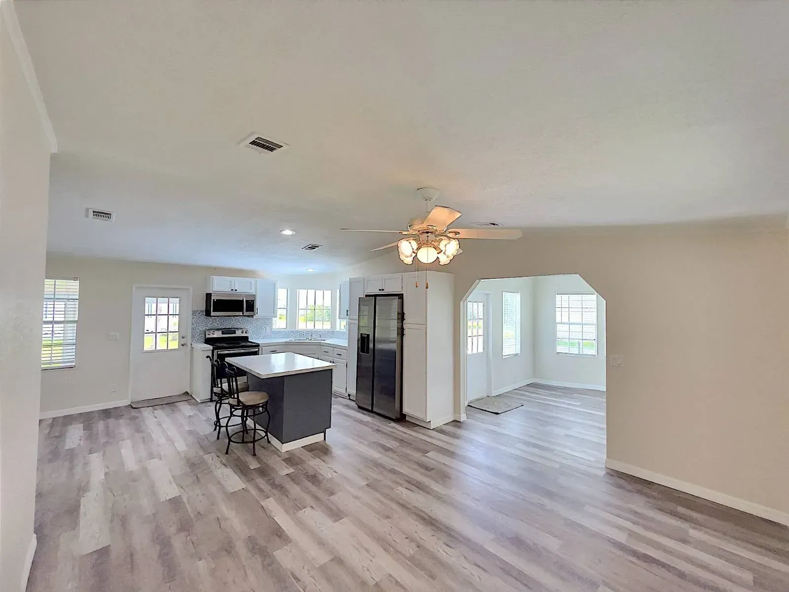 Open-concept living space with kitchen island, dark appliances, and light gray wood-look floors.