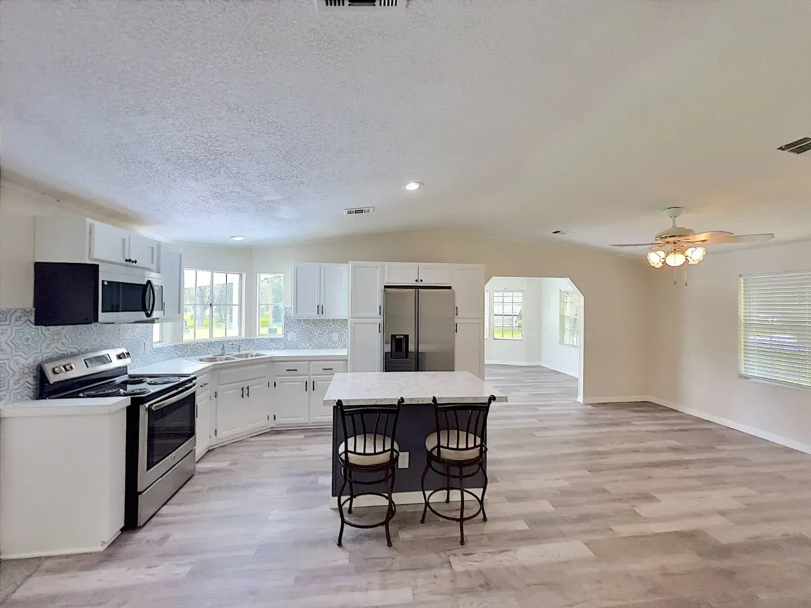 Bright kitchen with white cabinets, stainless steel appliances, and a kitchen island with two stools.