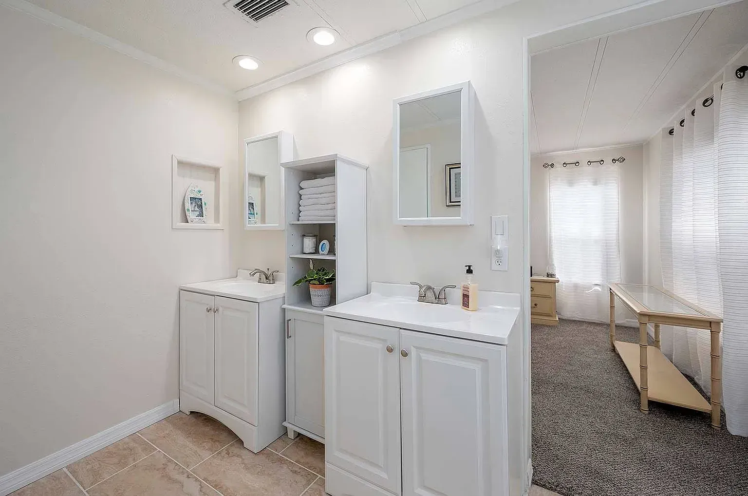Bathroom with white vanities, a storage cabinet, and a peek into a room with curtains.
