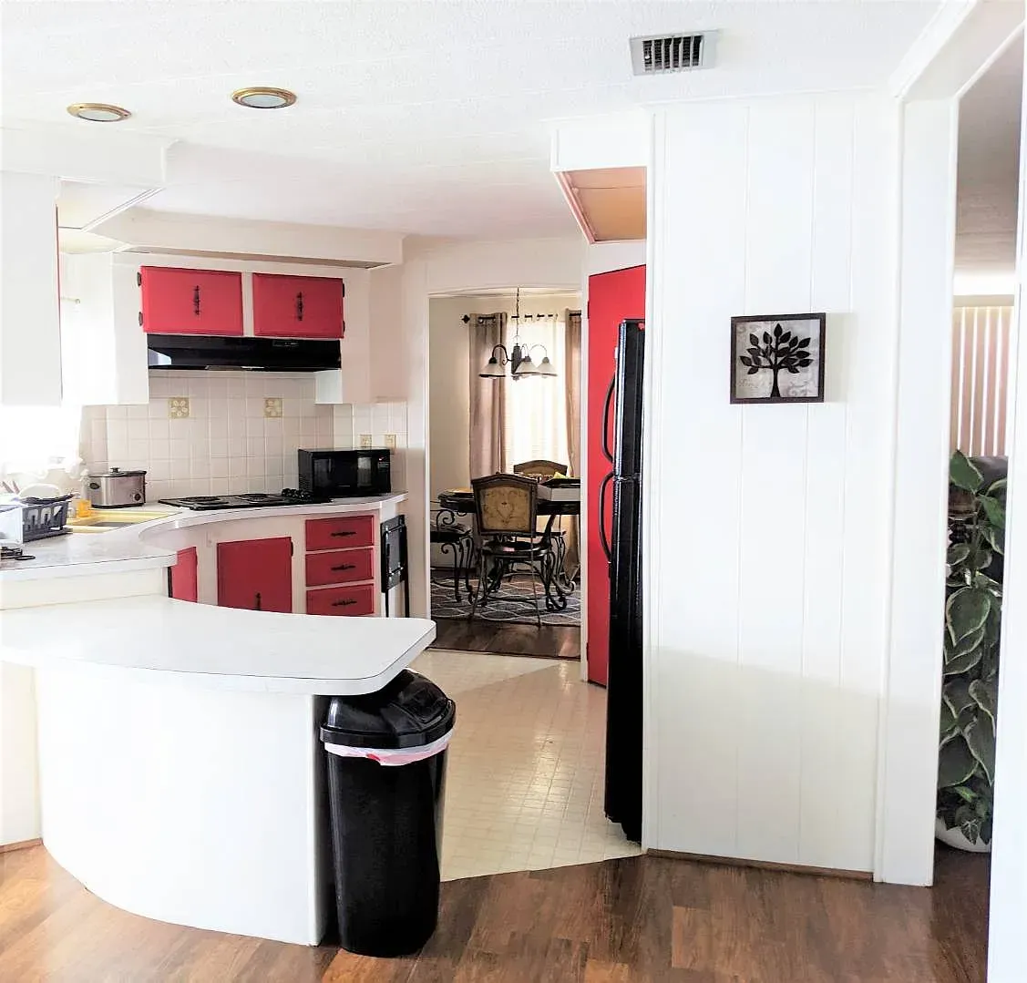 Kitchen with red cabinets and a white island, leading to a dining area.