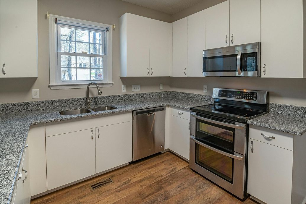 White kitchen with granite countertops, stainless steel appliances, and a window.
