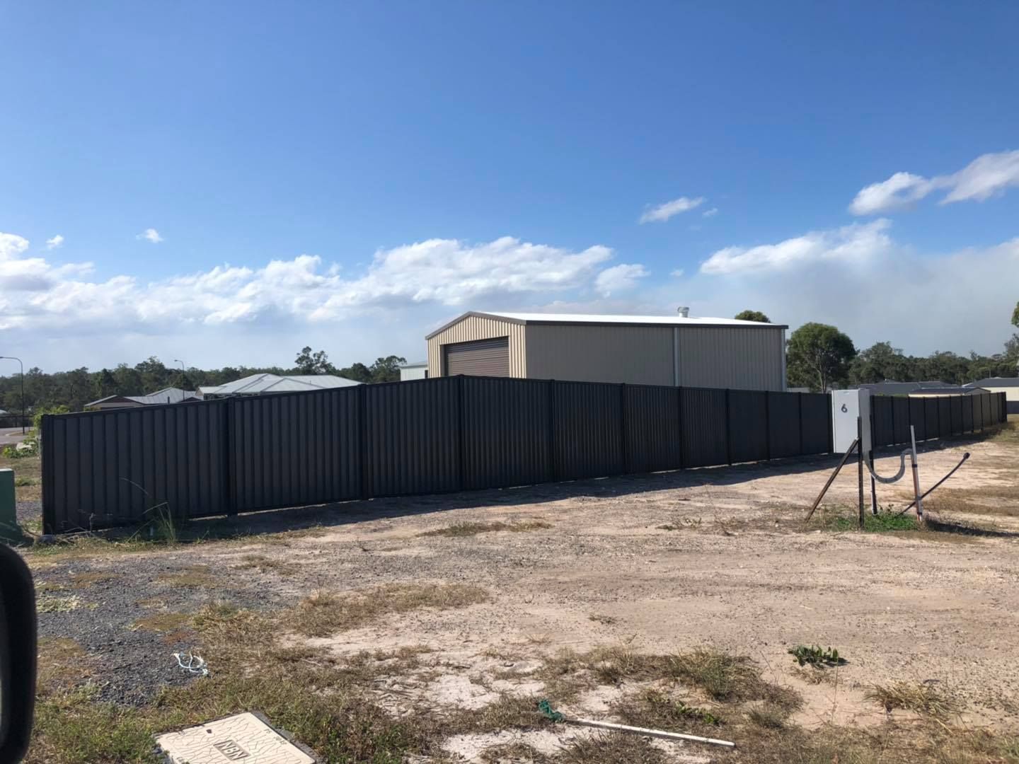 Large Fence Surrounds a Dirt Field With a Building in the Background — Lange's Fencing and Landscaping Centre in Island Plantation, QLD