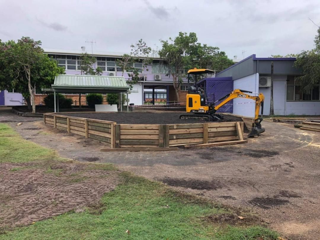 Yellow Excavator is Working on a Wooden Fence in Front of a Building — Lange's Fencing and Landscaping Centre in Island Plantation, QLD