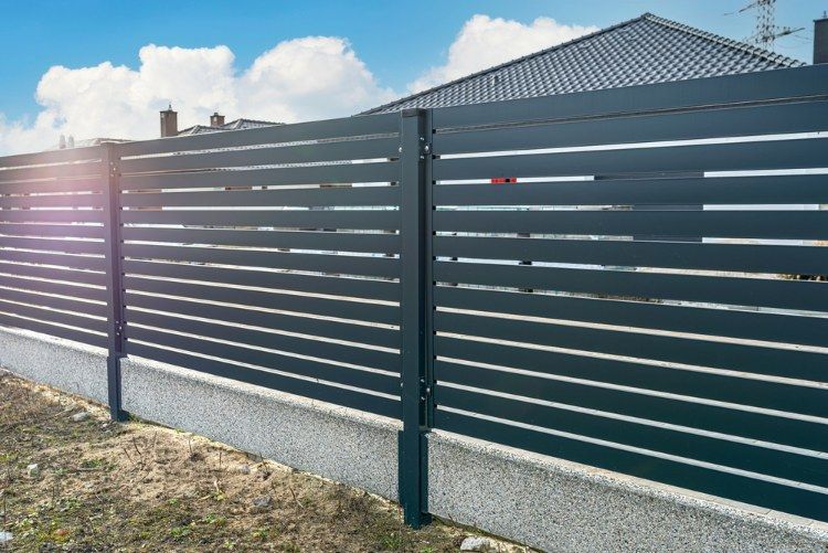 Black Fence is Surrounding a Concrete Wall in Front of a House — Lange's Fencing and Landscaping Centre in Island Plantation, QLD