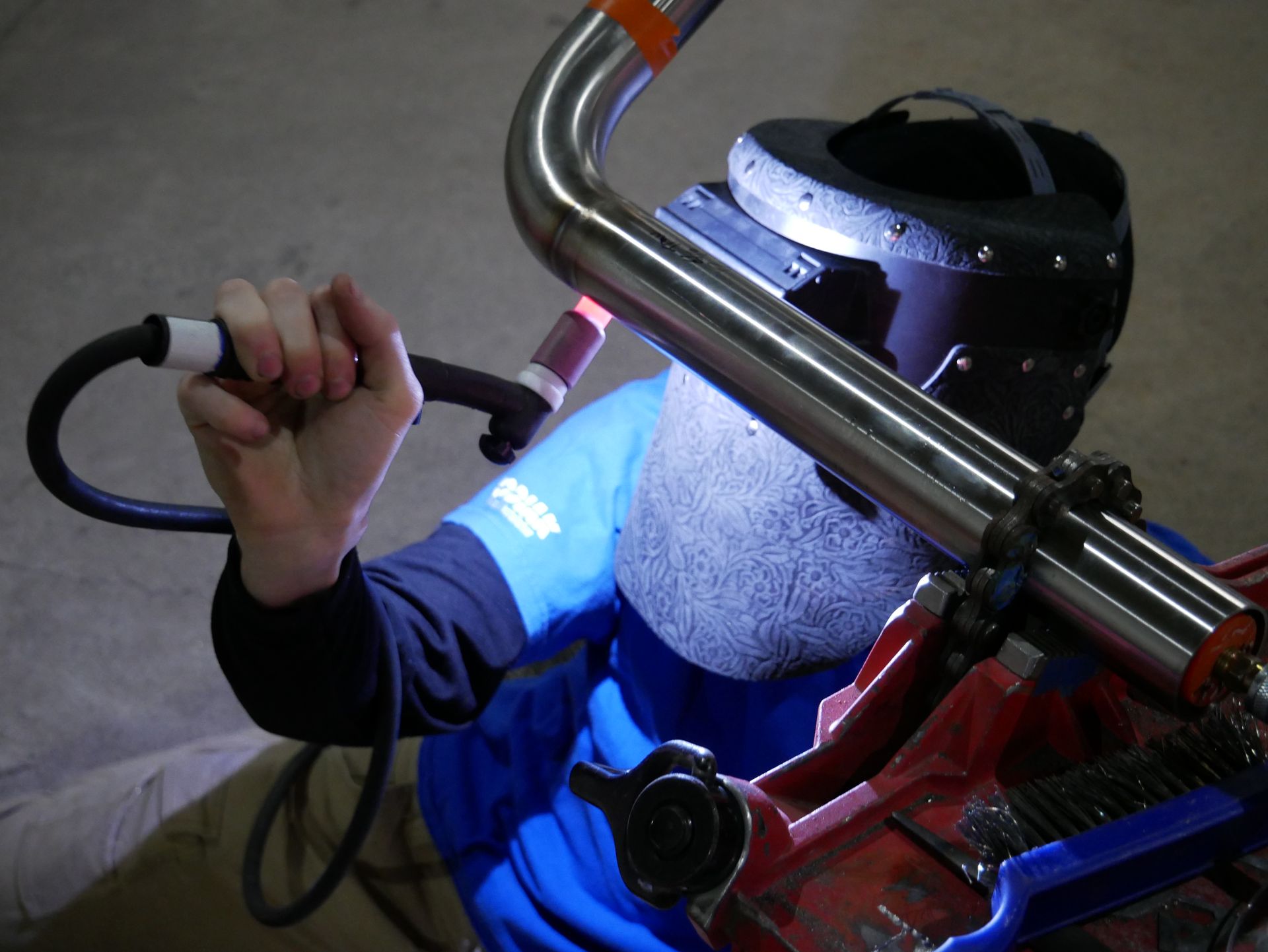 A man wearing a welding mask is welding a pipe