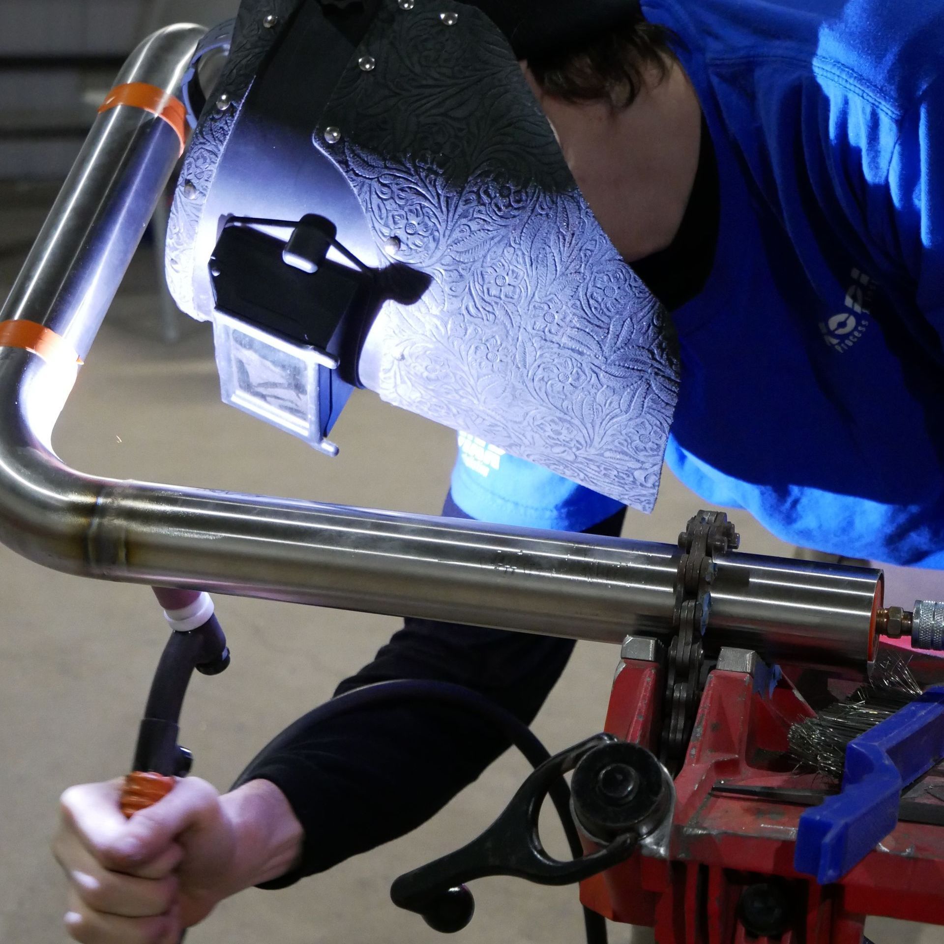 A man wearing a welding mask is working on a pipe