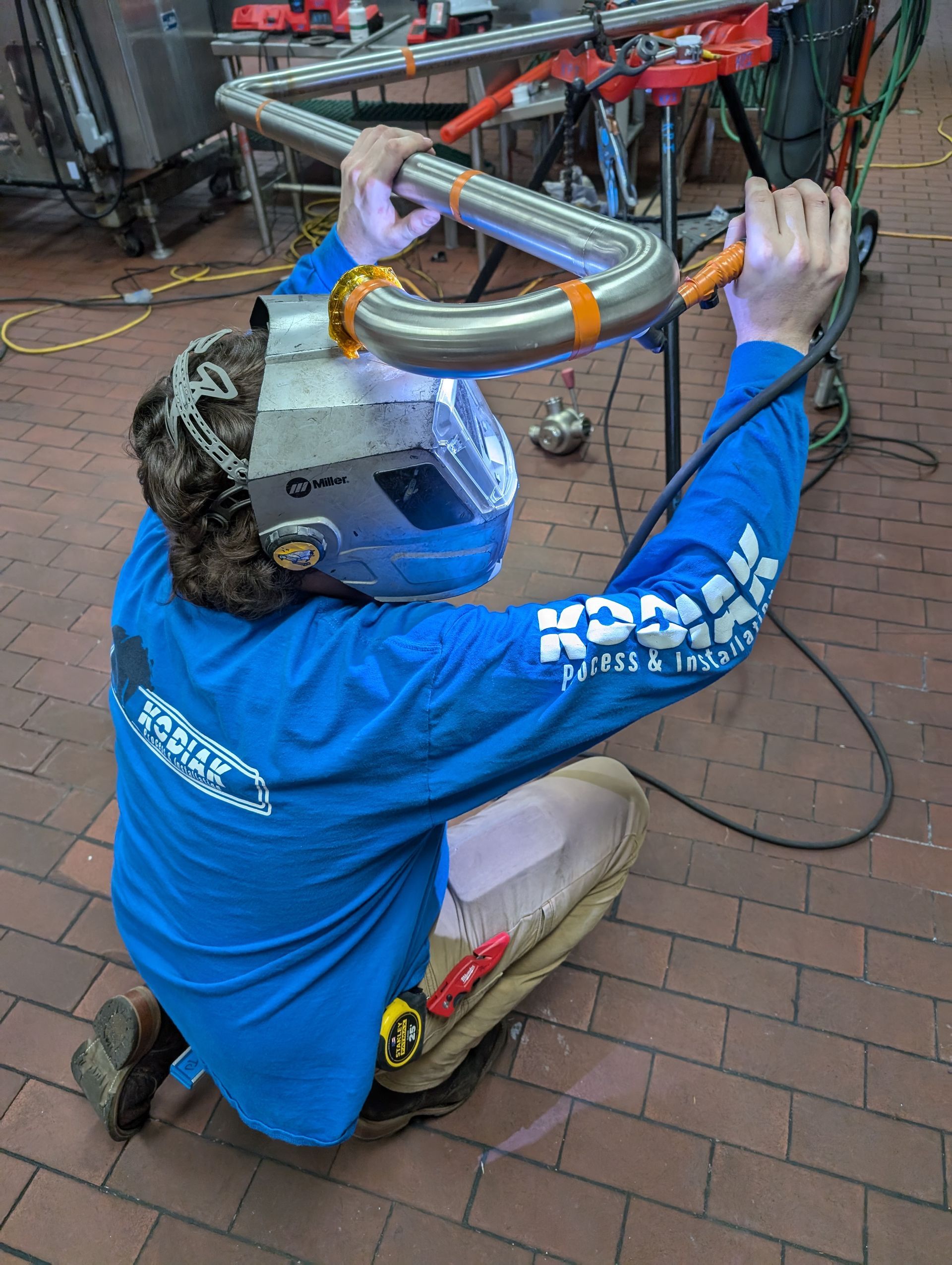 A man in a blue shirt is welding a pipe on a brick floor.