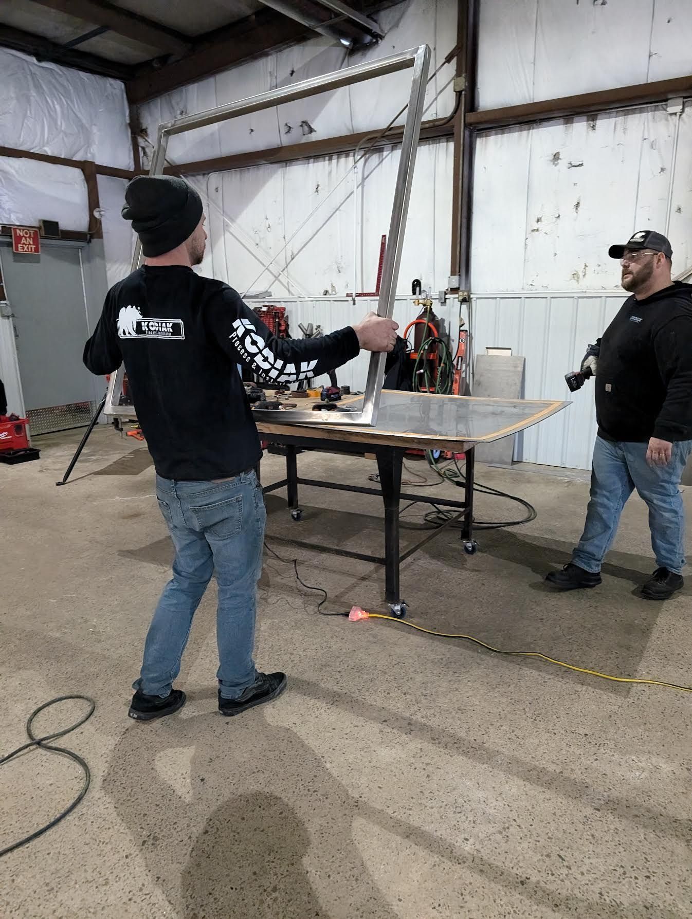 Two men are working on a piece of metal in a garage.