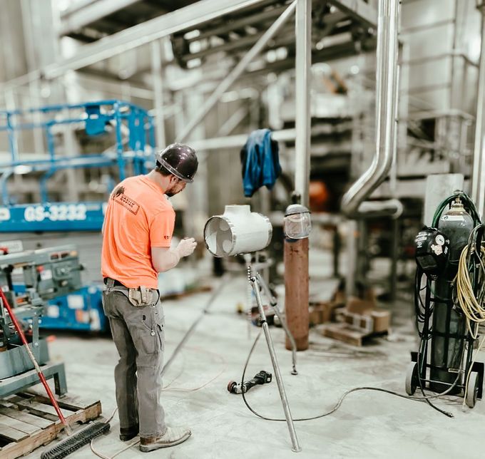 A man in an orange shirt is standing next to a lamp in a factory.
