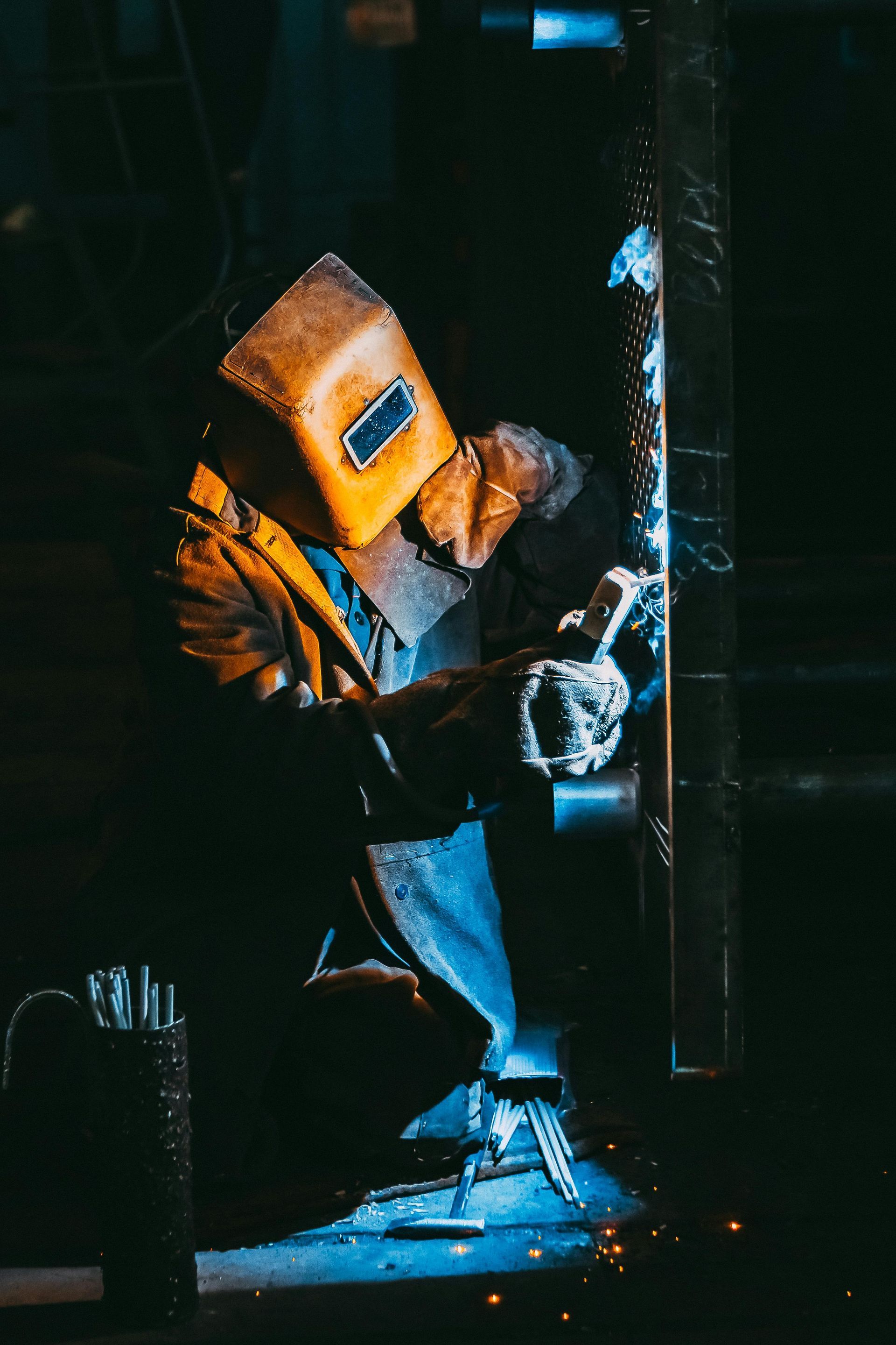 A man wearing a welding mask is welding a piece of metal.