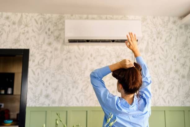 Woman holding hair near broken AC, showing need for emergency air conditioning service.