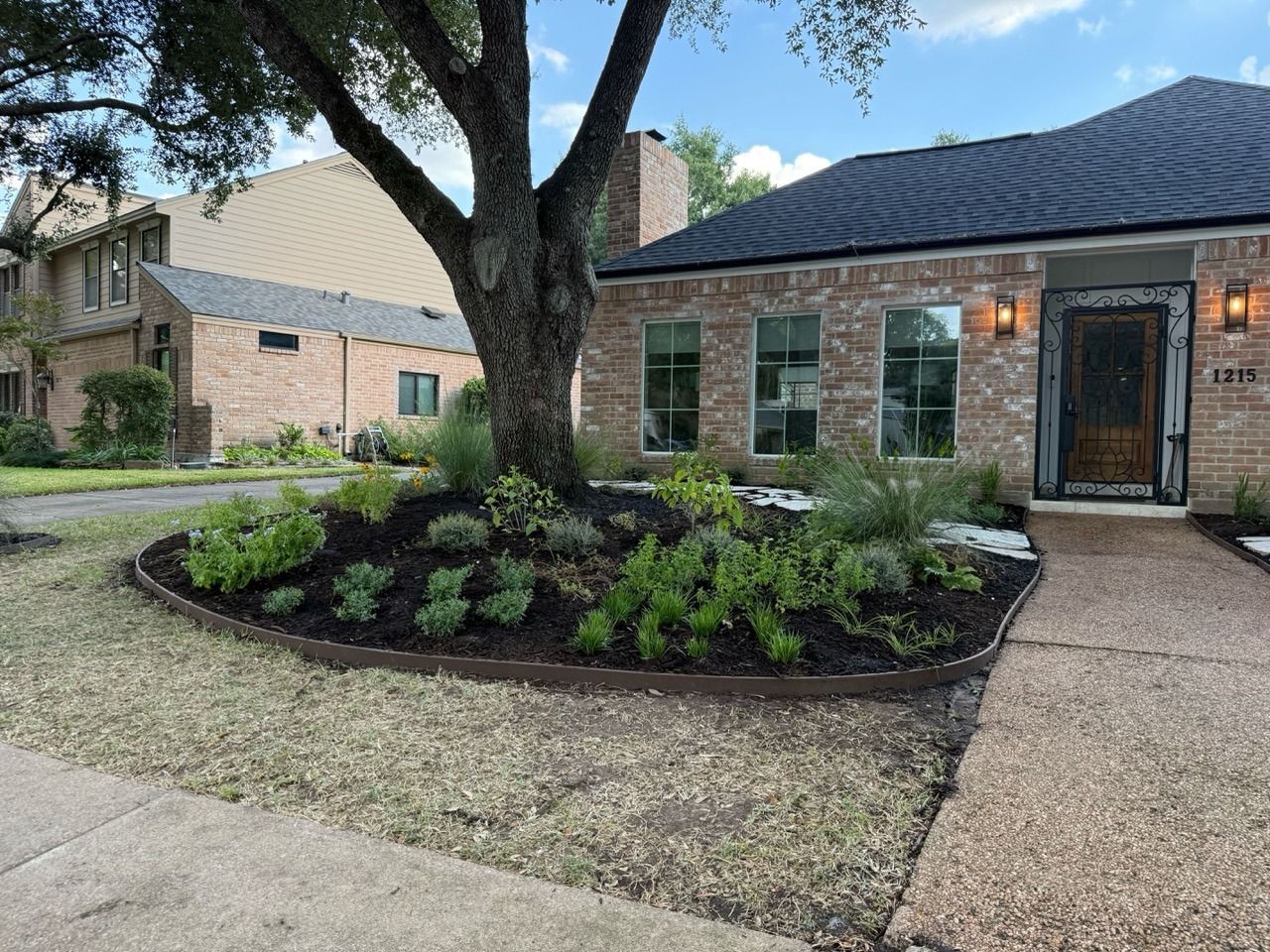 Brick house with dark roof, front walkway, and landscaped yard with a large tree and shrubs