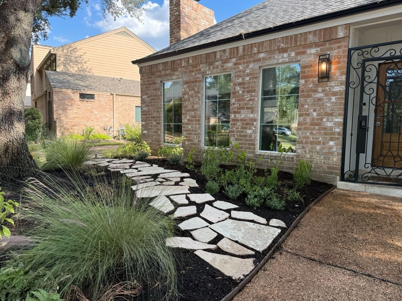 Brick house front entry with stone stepping path, landscaped grasses, and wrought-iron door
