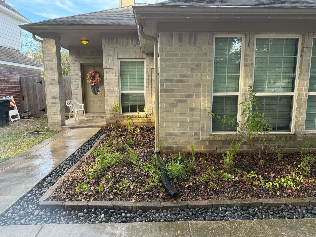 Front view of a beige house with a wet walkway, front door wreath, and small landscaped yard.