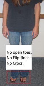 A woman wearing flip flops is standing in front of a sign that says no open toes no flip flops no crocs