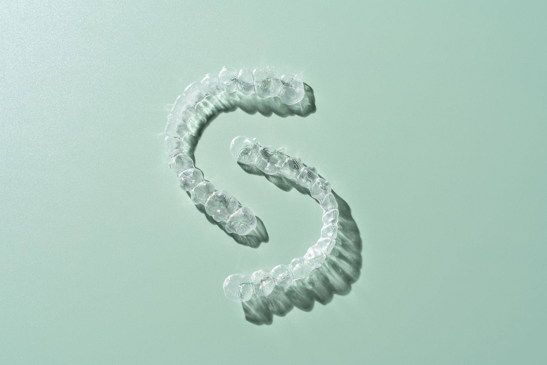 A pair of Invisalign braces on green background directly above view. A pair of Invisalign braces on green background directly above view.