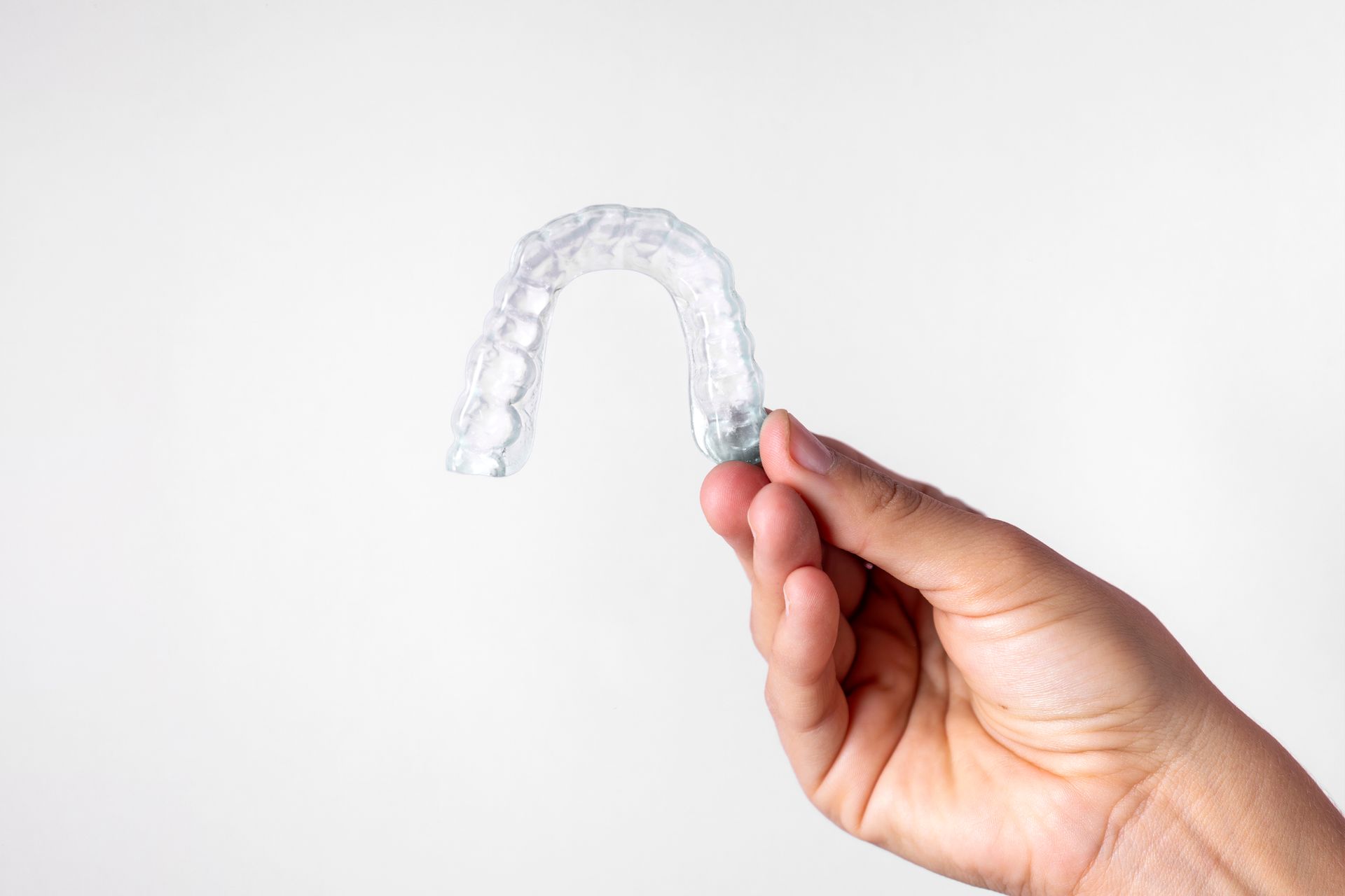 Hand holding clear Invisalign aligner against white background for teeth straightening.