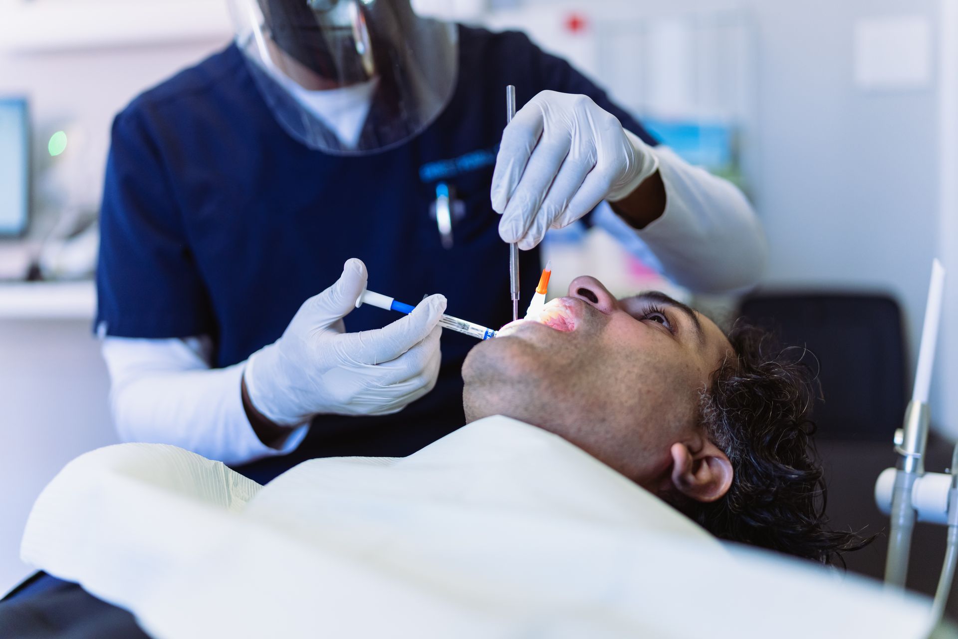 A male patient lies on a dental chair during a procedure done by a male dentist.