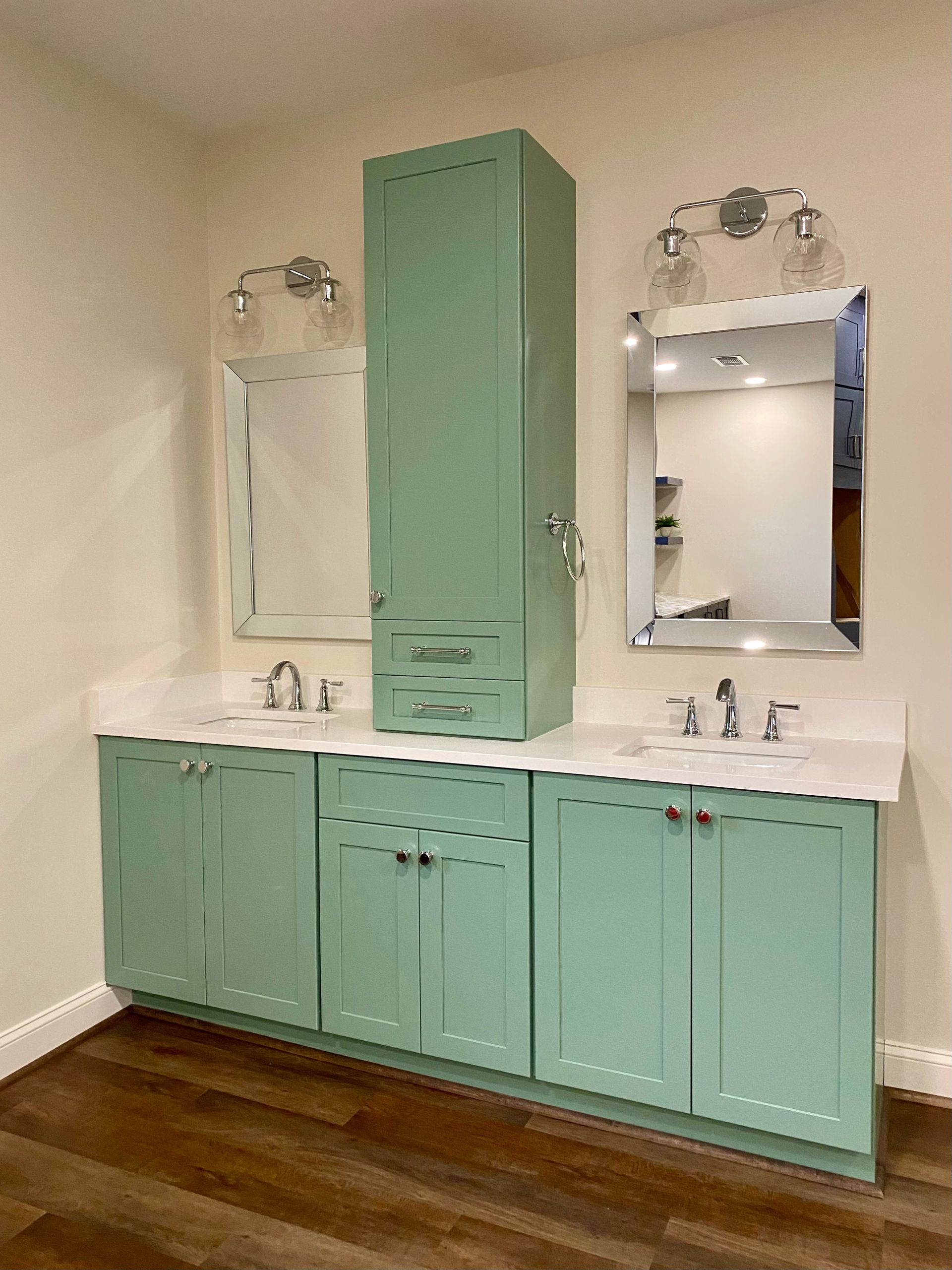 Bathroom with light green cabinets, a tall cabinet, white countertop, and mirrors.