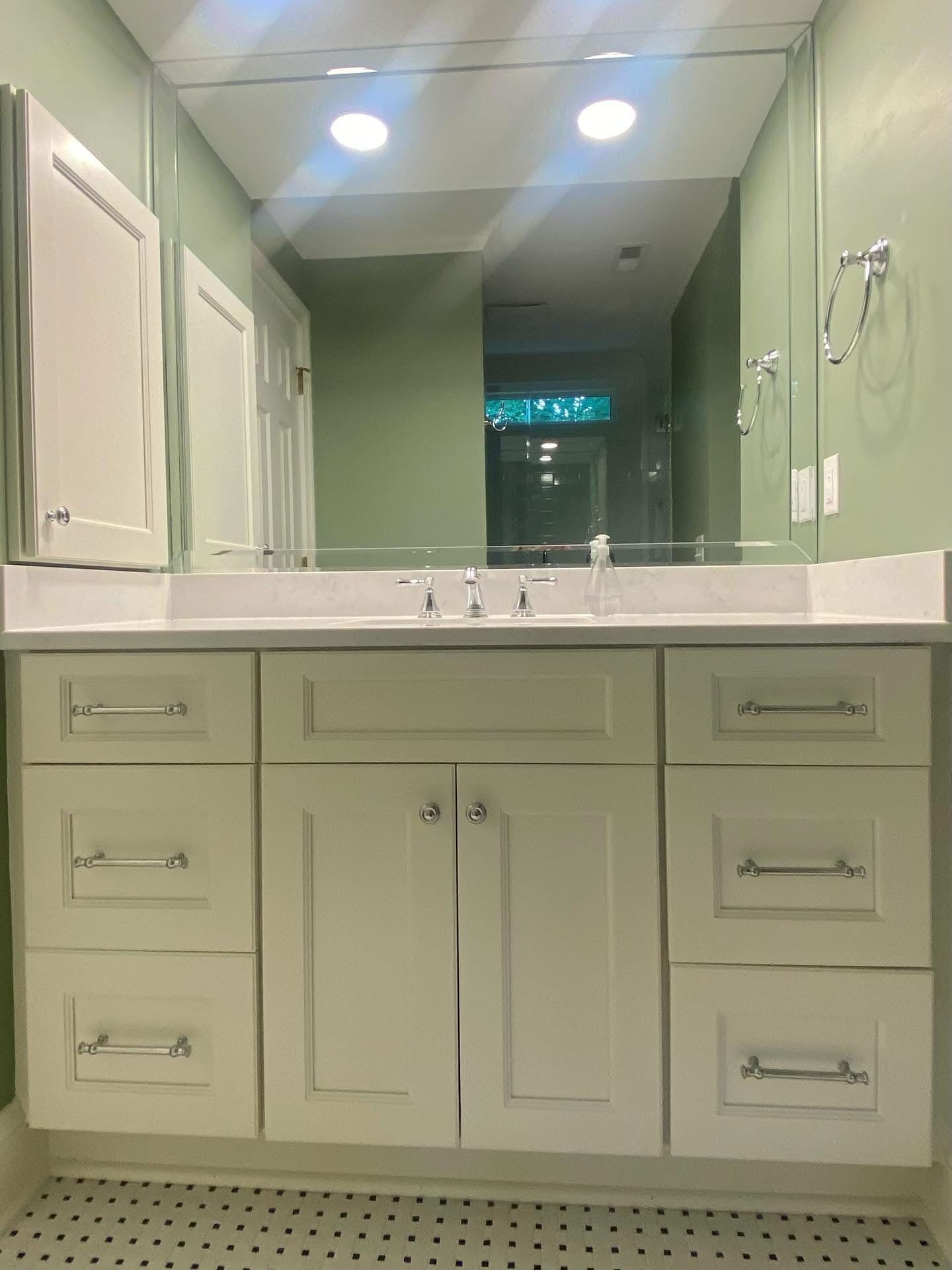 White bathroom vanity with drawers and cabinets, large mirror, and light green walls.