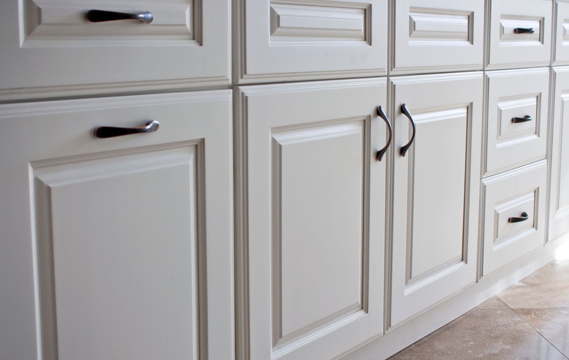 Close-up of white kitchen cabinets with black handles.