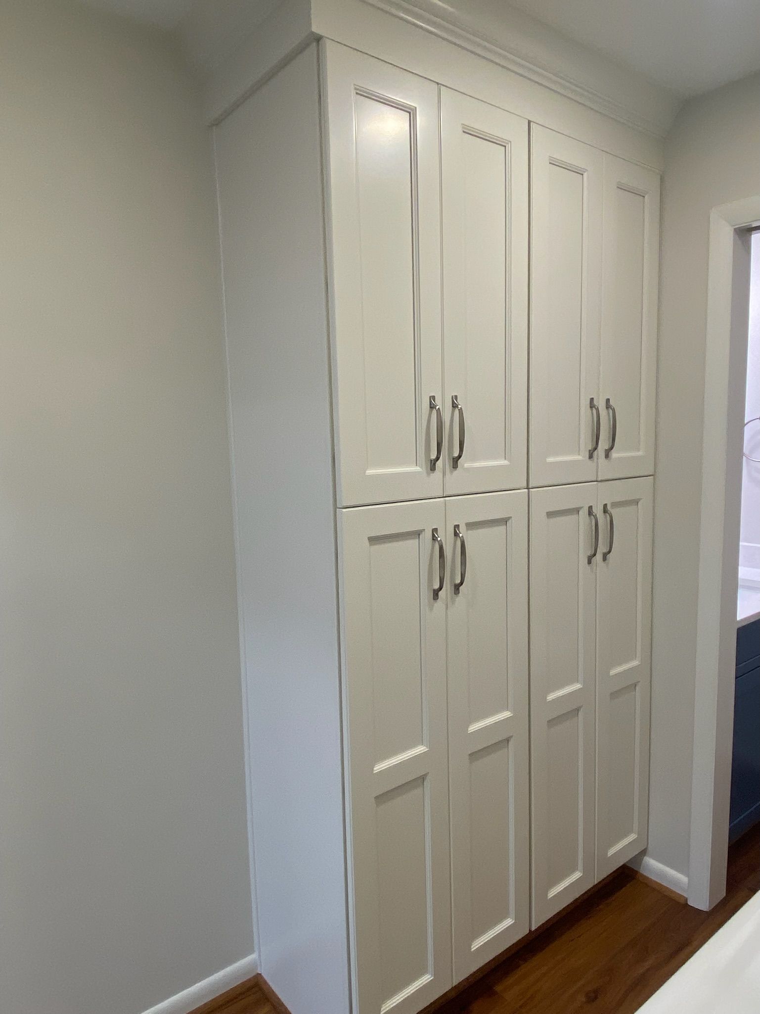 Tall white pantry cabinets with multiple doors and chrome handles against a wall.