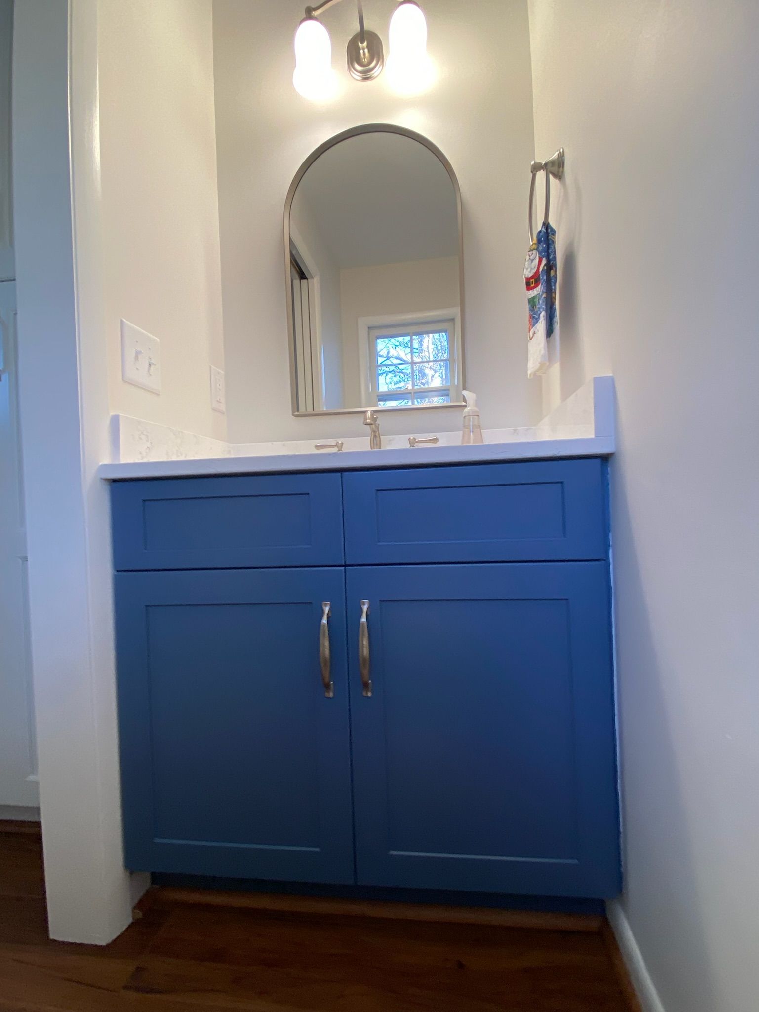 Blue bathroom vanity with arched mirror and sconce lighting.