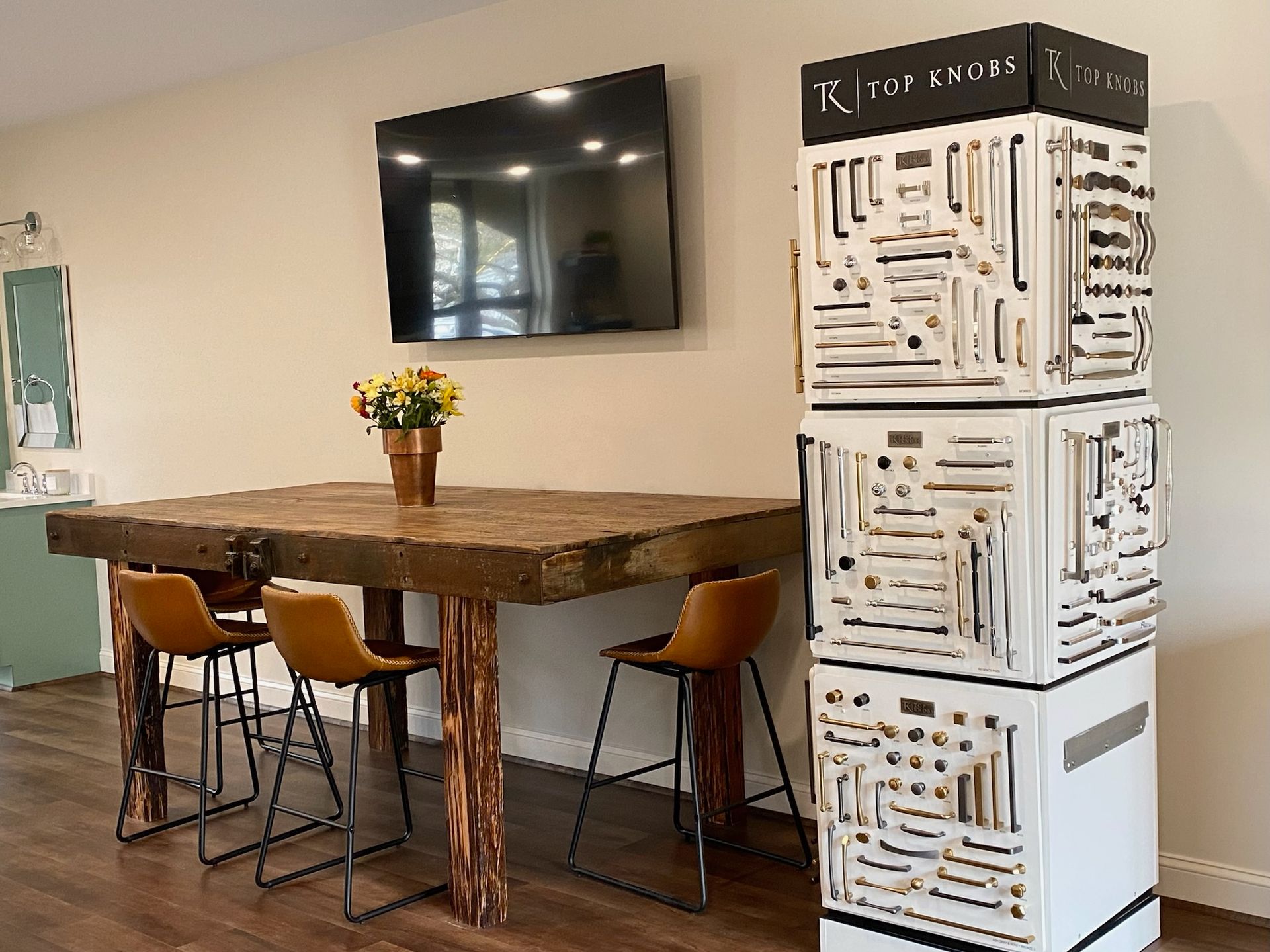 Wooden table with bar stools, TV, and display of cabinet hardware.
