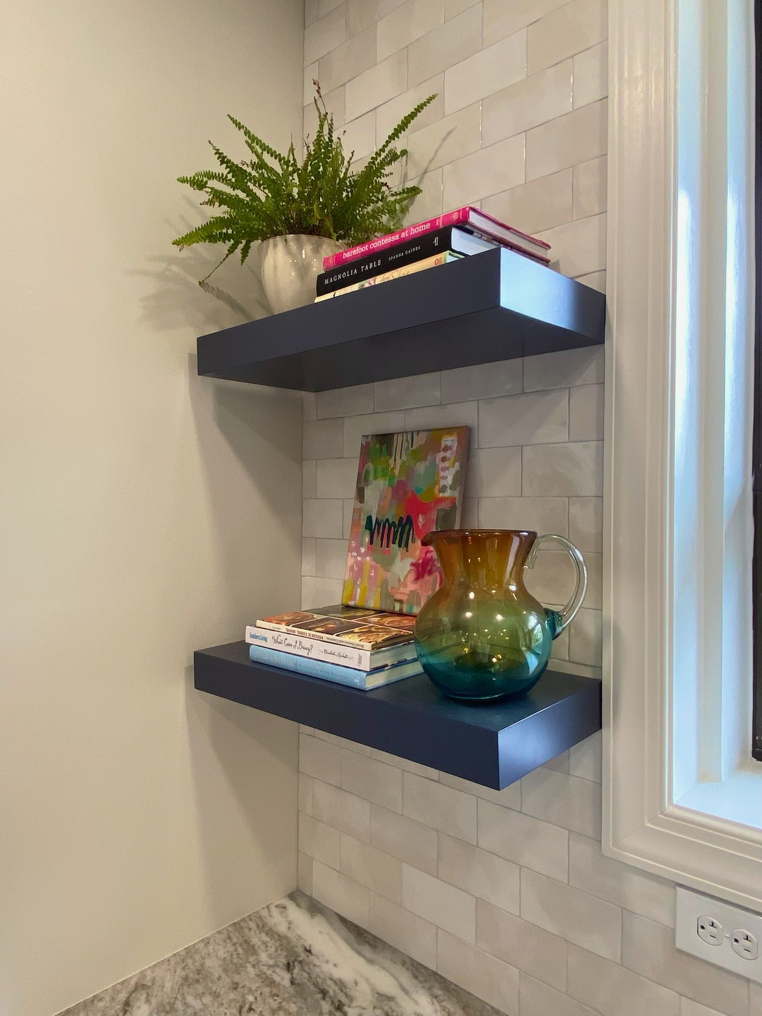 Two dark blue floating shelves with decor, against a light tile wall.