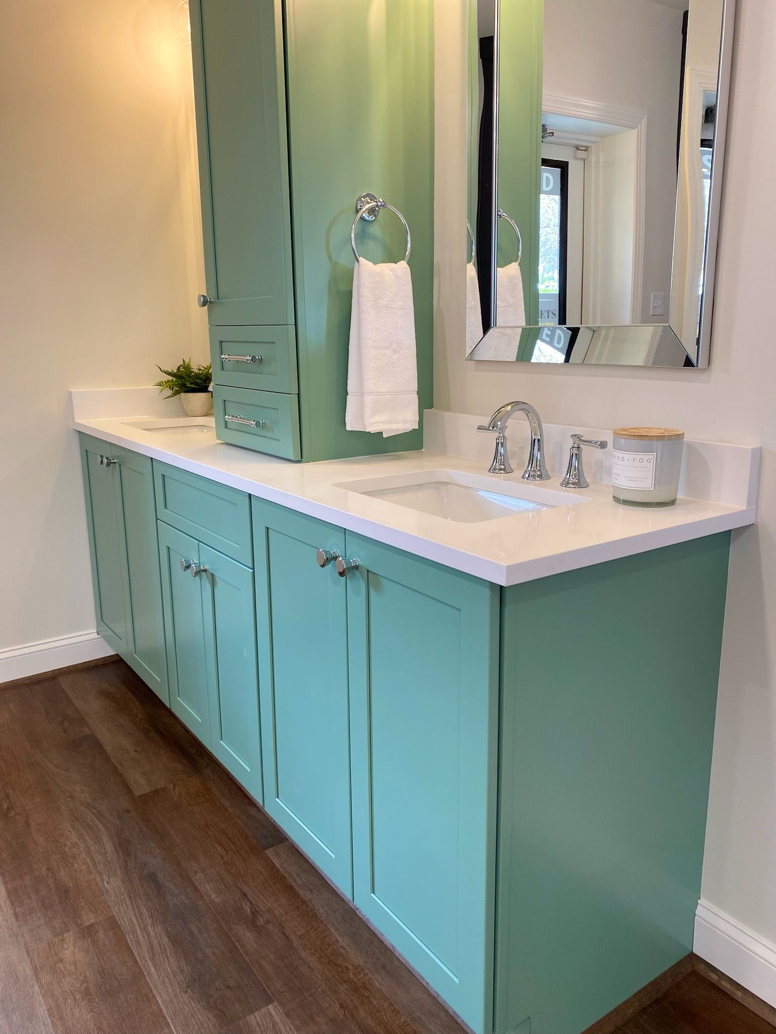 Mint-green bathroom vanity with white countertop and sink, tall matching cabinet, and mirror.
