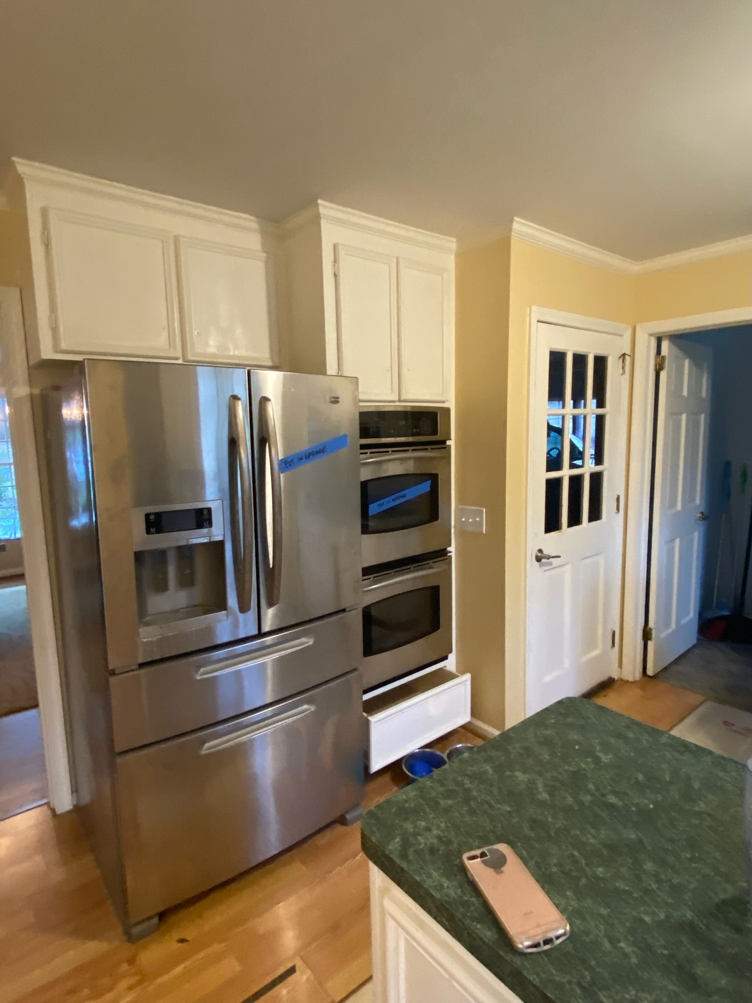 Stainless steel refrigerator and oven next to white cabinets in a kitchen with a green countertop.